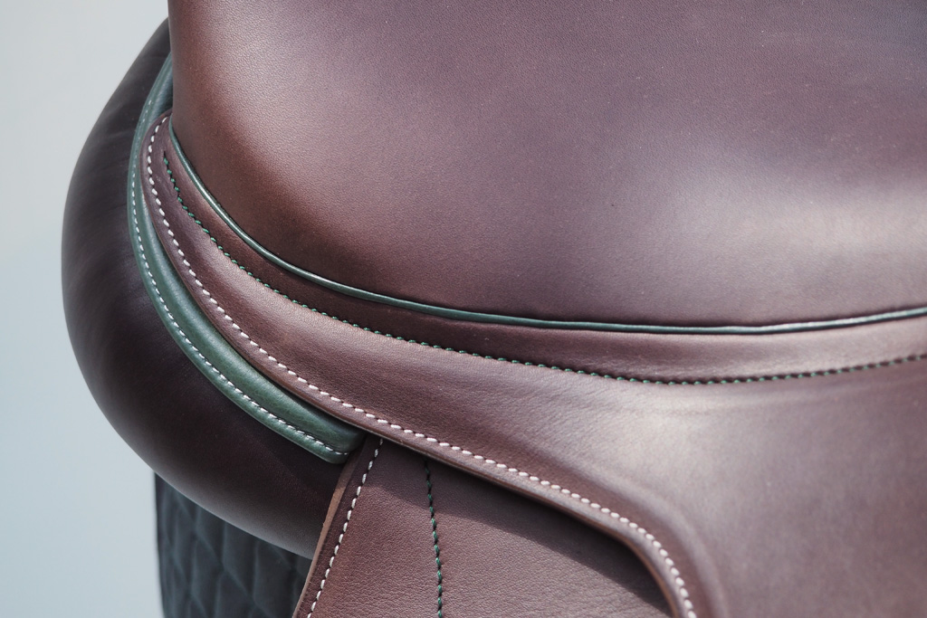 Détail d’une selle en cuir brun avec passepoil vert et couture main